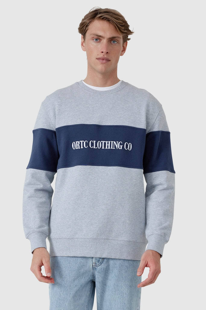 Male model wearing grey crew neck with navy middle panel with white embroidered ORTC Clothing co
