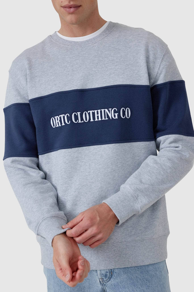 Close up of Male model wearing grey crew neck with navy middle panel with white embroidered ORTC Clothing co