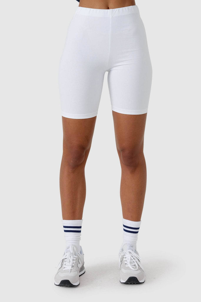 Female model wearing white bike shorts, white socks and new balance sneakers.