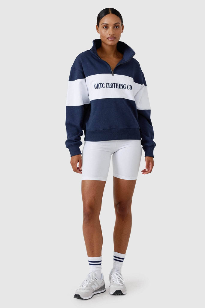 Female model wearing white bike shorts with a navy and white quarter zip jumper