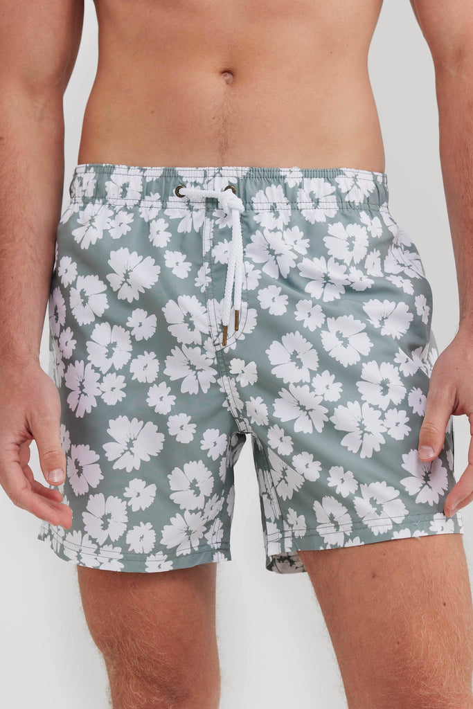 Model wearing sage board shorts with white flowers on them