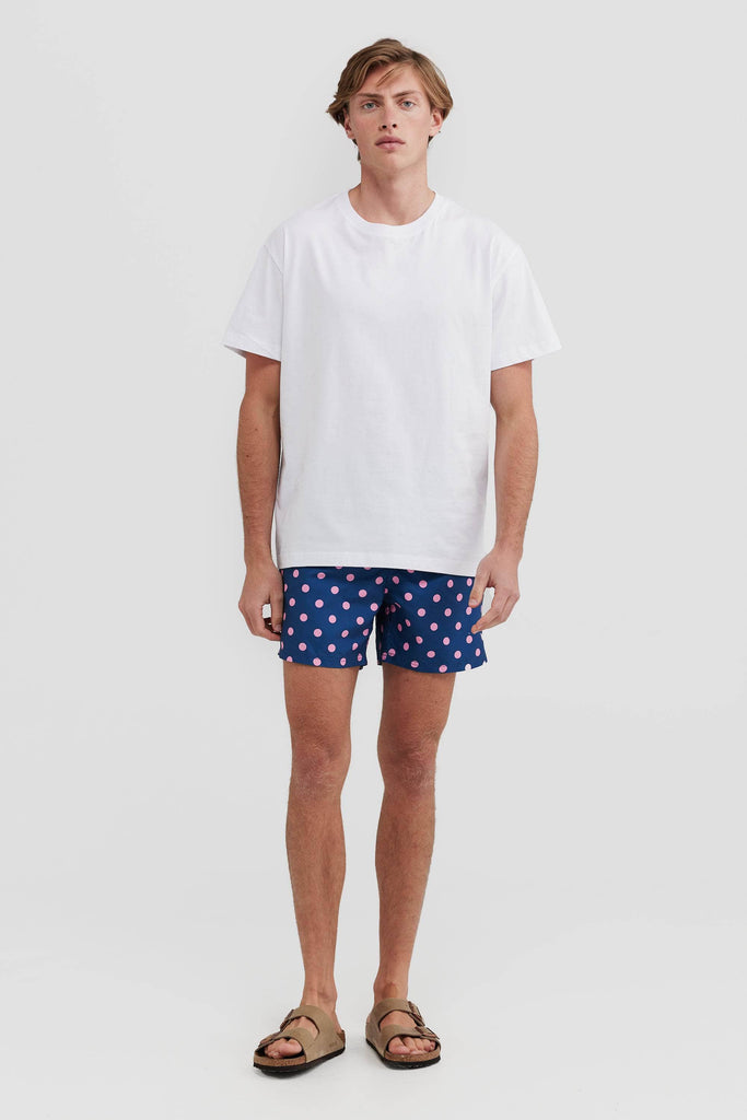 Full length of model wearing a white tshirt, navy board shorts with pink polka dots and birkenstocks.