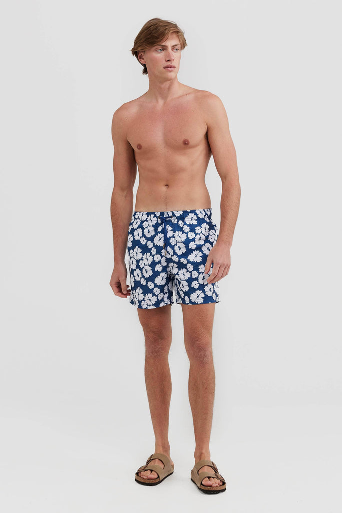 Model wearing Blue with white flowers board shorts. He's not wearing a top and has birkenstocks on.