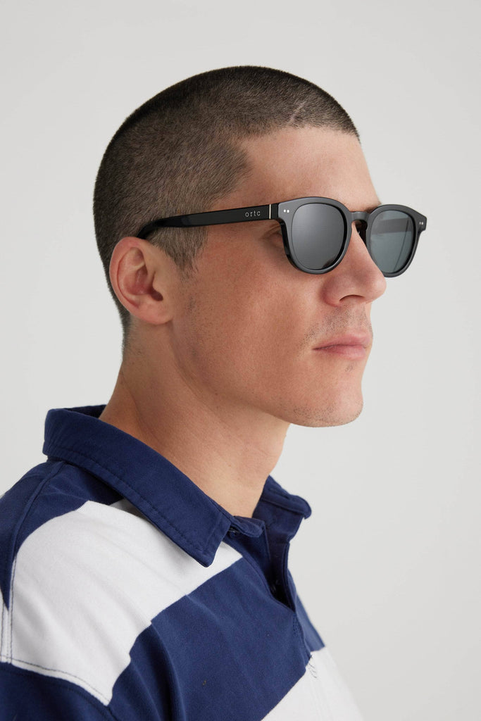 Model wearing black framed sunglasses with ortc on the arm