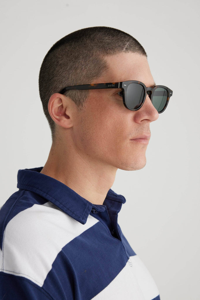 Model wearing tortoiseshell sunglasses with white ortc logo on arm